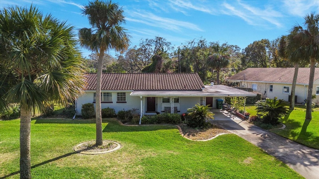 view of front of house featuring an attached carport, concrete driveway, a tile roof, and a front lawn