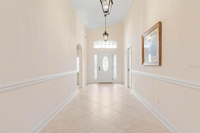 tiled foyer with arched walkways, a high ceiling, and baseboards