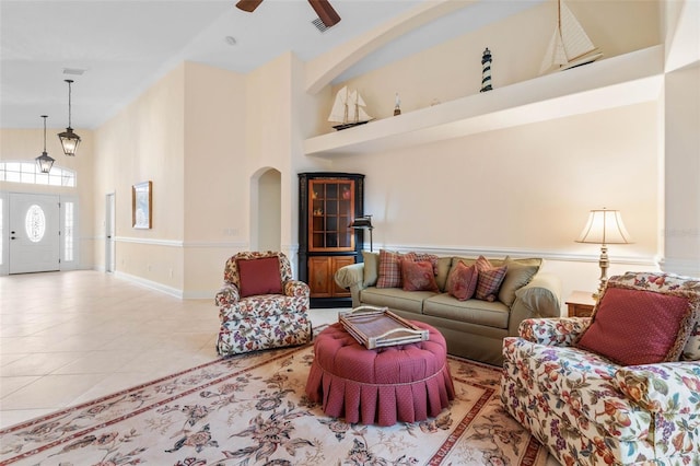 living area featuring arched walkways, tile patterned flooring, visible vents, a towering ceiling, and a ceiling fan