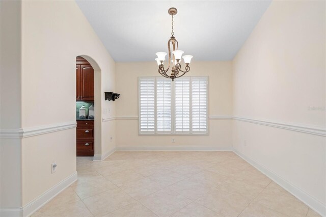 empty room with baseboards, arched walkways, vaulted ceiling, a notable chandelier, and light tile patterned flooring