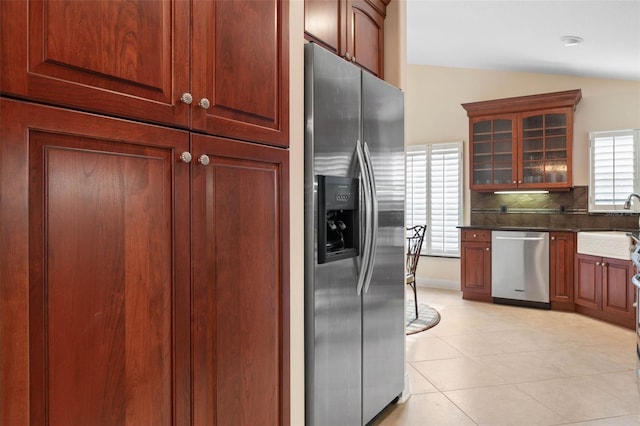 kitchen with light tile patterned floors, lofted ceiling, decorative backsplash, appliances with stainless steel finishes, and glass insert cabinets