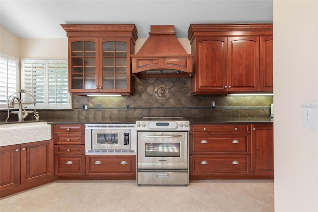 kitchen featuring decorative backsplash, dark stone counters, appliances with stainless steel finishes, custom exhaust hood, and a sink