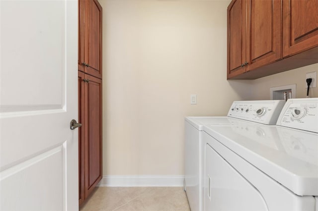 laundry area with light tile patterned flooring, washing machine and dryer, cabinet space, and baseboards