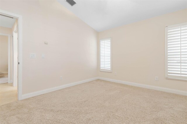 empty room featuring lofted ceiling, baseboards, visible vents, and light colored carpet