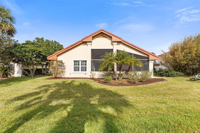 back of house with a sunroom, a tile roof, a lawn, and stucco siding