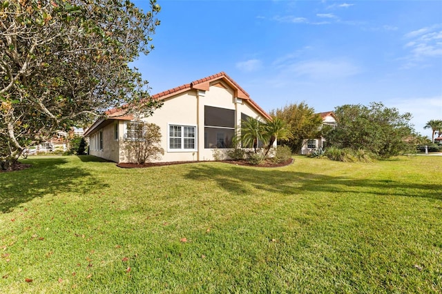 view of side of home with a lawn, a tile roof, and stucco siding