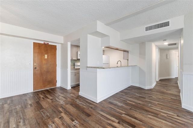 kitchen with dark wood-style flooring, a wainscoted wall, visible vents, freestanding refrigerator, and a sink