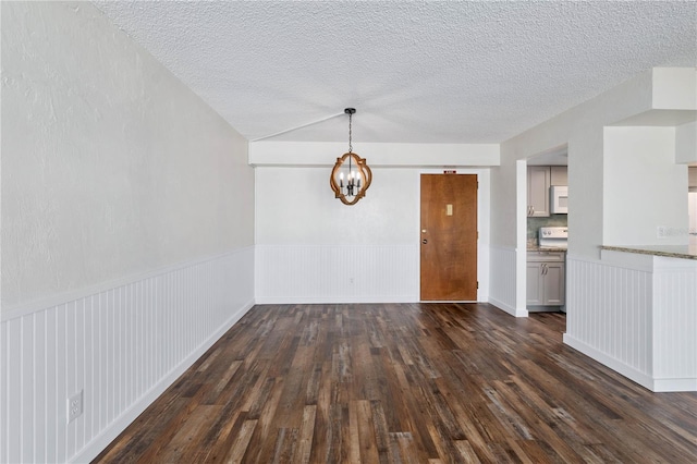 unfurnished dining area featuring a wainscoted wall, dark wood-type flooring, a textured ceiling, and a notable chandelier