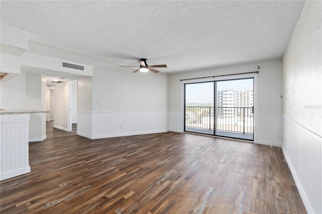 unfurnished room with dark wood-type flooring, a wainscoted wall, visible vents, and ceiling fan