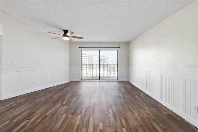 unfurnished room with dark wood-style floors, a wainscoted wall, a textured ceiling, and a ceiling fan