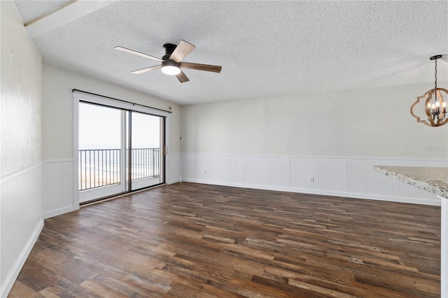 empty room with a wainscoted wall, dark wood finished floors, a textured ceiling, and ceiling fan with notable chandelier