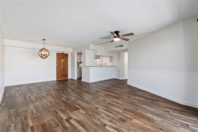 unfurnished living room with a wainscoted wall, dark wood finished floors, visible vents, a textured ceiling, and ceiling fan with notable chandelier