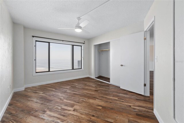 unfurnished bedroom featuring a textured ceiling, a closet, dark wood finished floors, and baseboards