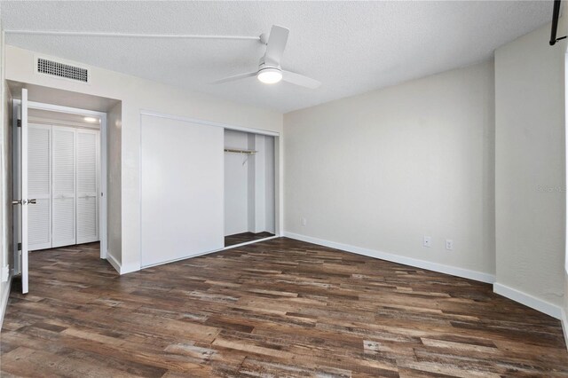 unfurnished bedroom featuring a textured ceiling, visible vents, dark wood finished floors, and a closet