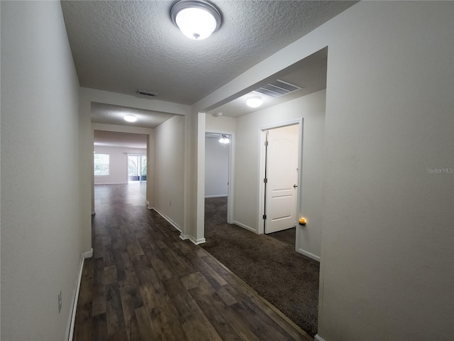 hallway with visible vents, dark wood finished floors, a textured ceiling, and baseboards