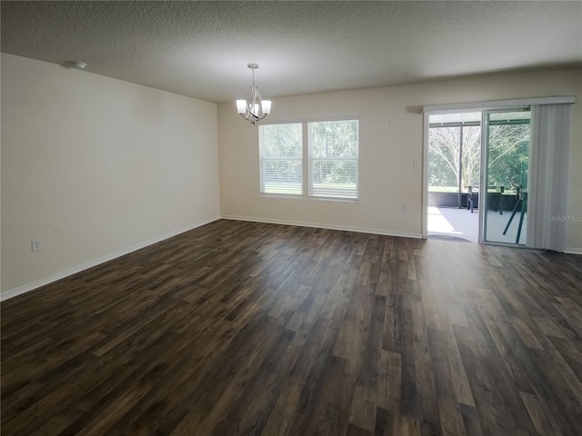 empty room featuring a notable chandelier, a textured ceiling, baseboards, and dark wood-type flooring