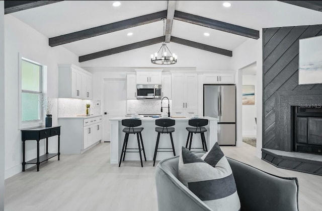 kitchen with a breakfast bar area, appliances with stainless steel finishes, vaulted ceiling with beams, light countertops, and a notable chandelier