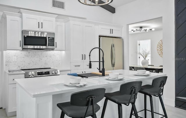 kitchen featuring stainless steel appliances, visible vents, white cabinets, tasteful backsplash, and an island with sink