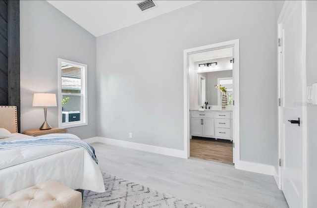 bedroom with a sink, visible vents, baseboards, light wood finished floors, and ensuite bath