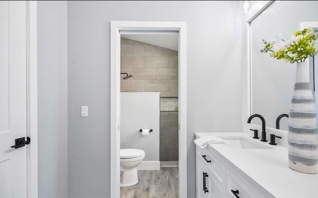 bathroom with toilet, tiled shower, wood finished floors, and vanity