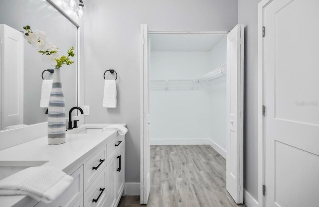 full bath featuring a spacious closet, wood finished floors, vanity, and baseboards