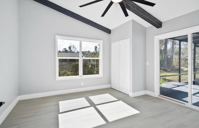 empty room featuring lofted ceiling with beams, ceiling fan, wood finished floors, and baseboards