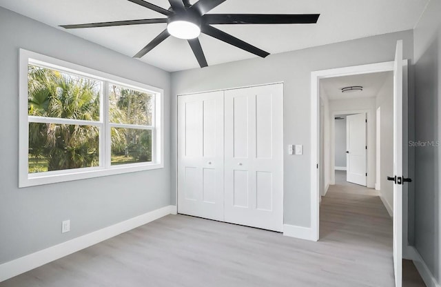 unfurnished bedroom featuring ceiling fan, a closet, light wood-style flooring, and baseboards