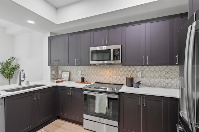 kitchen featuring light countertops, decorative backsplash, appliances with stainless steel finishes, a sink, and light wood-type flooring