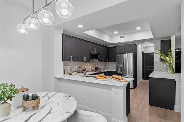 kitchen with stainless steel appliances, light wood finished floors, a raised ceiling, and light countertops