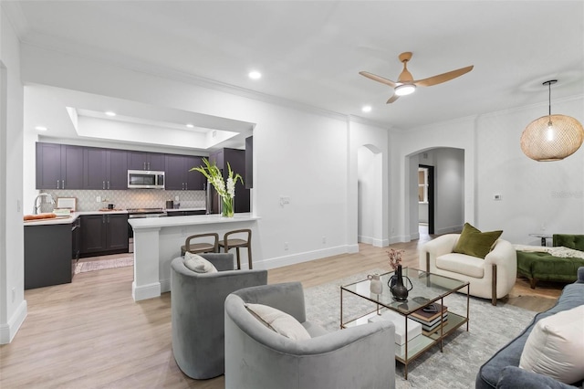 living room featuring arched walkways, recessed lighting, baseboards, light wood-style floors, and ornamental molding