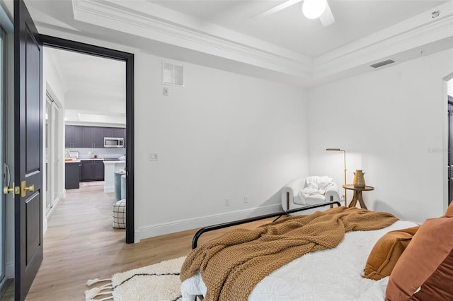 bedroom featuring light wood finished floors, baseboards, visible vents, a raised ceiling, and crown molding