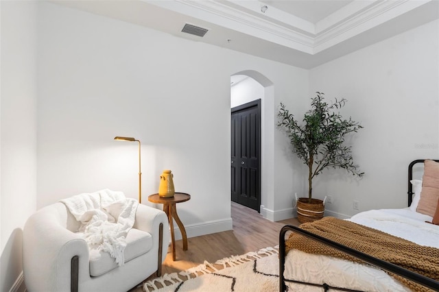 bedroom with baseboards, visible vents, arched walkways, wood finished floors, and crown molding