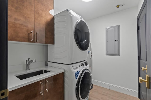 laundry area featuring a sink, light wood-style floors, stacked washing maching and dryer, cabinet space, and electric panel