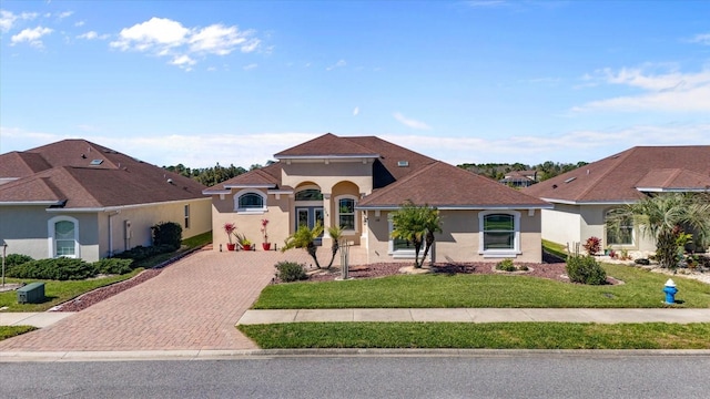 mediterranean / spanish-style home with a front yard, decorative driveway, and stucco siding