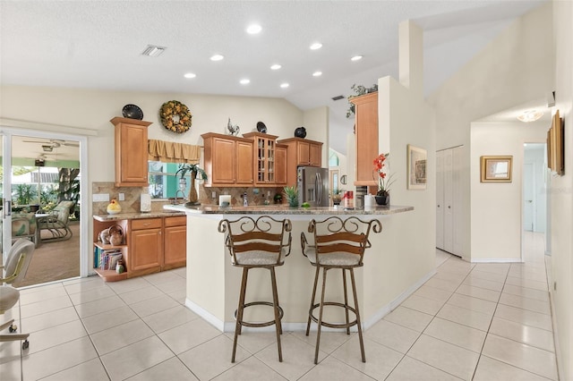 33 Poinsettia Ln, Palm Coast, FL 32164 - kitchen featuring stainless steel refrigerator with ice dispenser, decorative backsplash, a peninsula, glass insert cabinets, and a kitchen breakfast bar