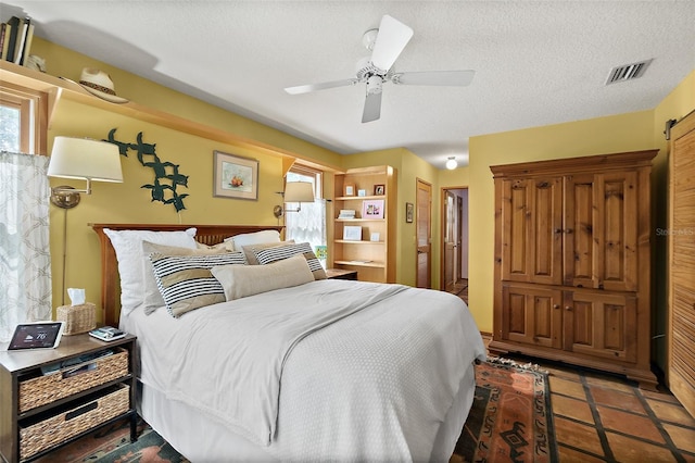 tiled bedroom featuring a textured ceiling, multiple windows, visible vents, and a ceiling fan