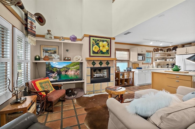 living area featuring light tile patterned flooring, a towering ceiling, visible vents, a tiled fireplace, and track lighting