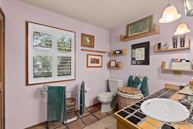 bathroom with a textured ceiling, toilet, a sink, baseboards, and tile patterned floors