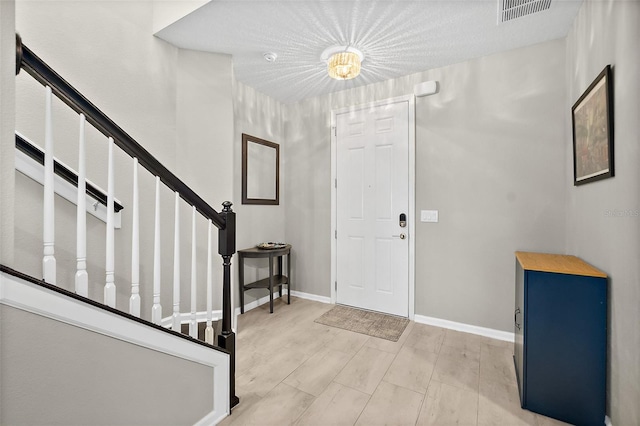 foyer featuring visible vents, baseboards, and stairs