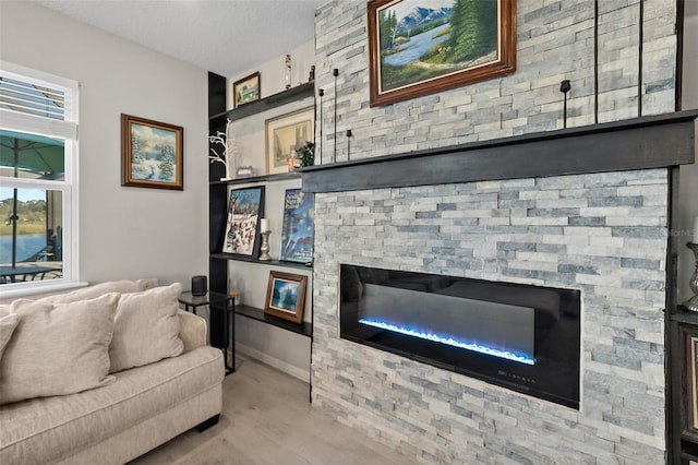 living area featuring a stone fireplace, a textured ceiling, and wood finished floors