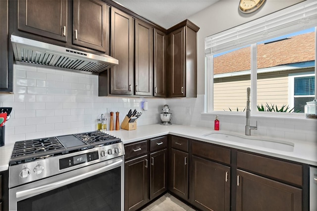 kitchen featuring stainless steel range with gas cooktop, tasteful backsplash, a sink, dark brown cabinetry, and under cabinet range hood