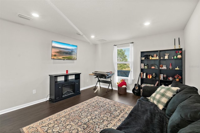 living area with baseboards, visible vents, wood finished floors, and a glass covered fireplace