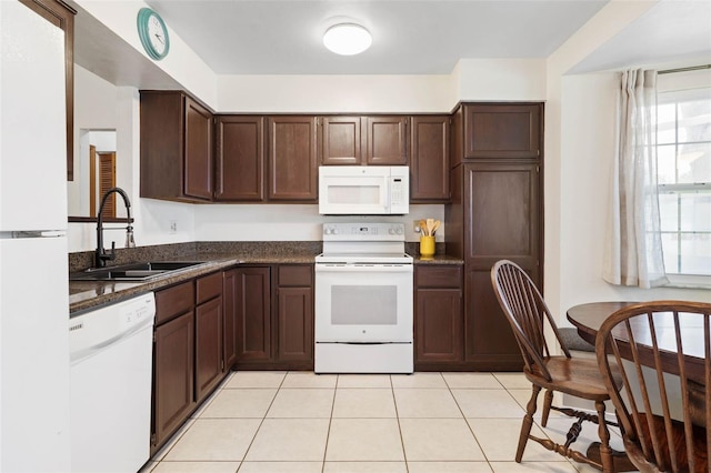 kitchen featuring dark brown cabinetry, white appliances, light tile patterned floors, and a sink