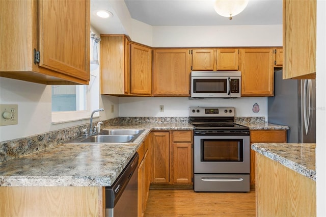 kitchen featuring appliances with stainless steel finishes, brown cabinets, a sink, and light wood finished floors