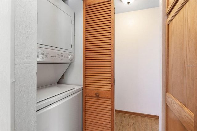 laundry room featuring laundry area, light wood-style flooring, stacked washer and clothes dryer, and baseboards