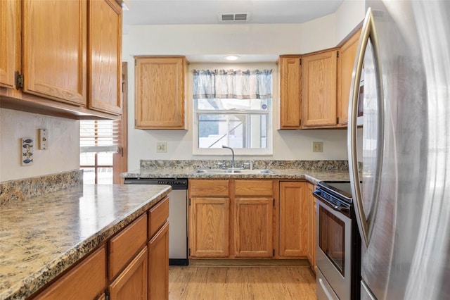 kitchen featuring light wood finished floors, visible vents, light stone countertops, stainless steel appliances, and a sink