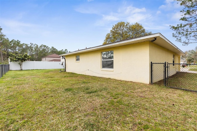 rear view of house featuring a yard, fence, and stucco siding