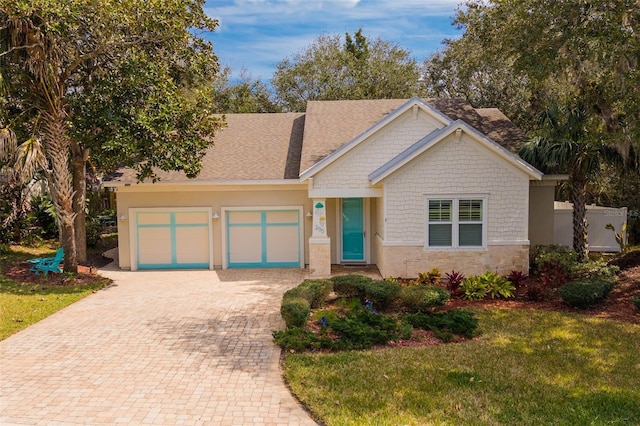 view of front of home with a front yard, decorative driveway, stone siding, and an attached garage