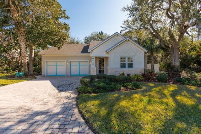 craftsman-style house featuring stone siding, a front lawn, decorative driveway, and a garage