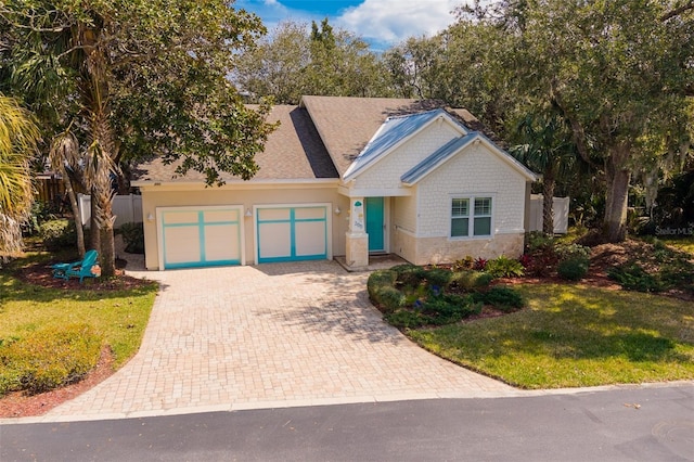 view of front of property featuring a front lawn, decorative driveway, stone siding, fence, and a garage